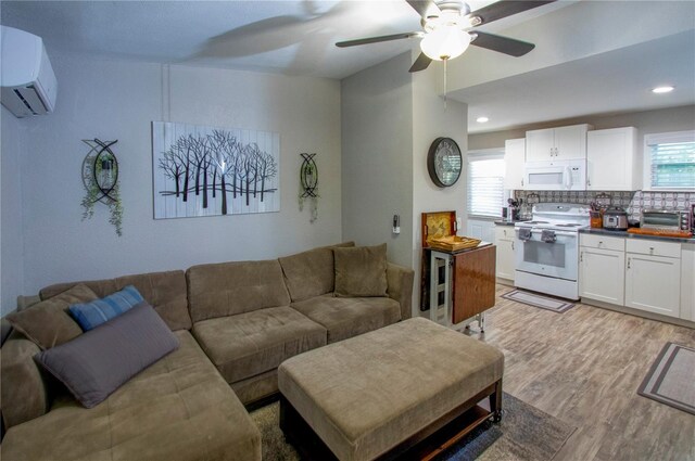 living room featuring light wood-style floors, an AC wall unit, a healthy amount of sunlight, and ceiling fan