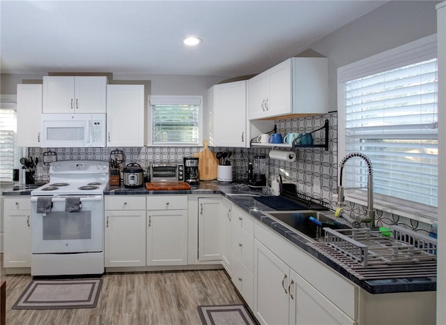 kitchen with light wood-type flooring, white appliances, dark countertops, and white cabinetry