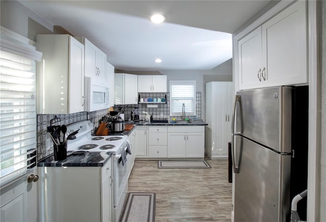 kitchen featuring dark countertops, white appliances, white cabinets, and a sink