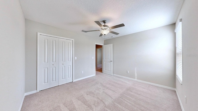 unfurnished bedroom with ceiling fan, light carpet, a closet, and a textured ceiling