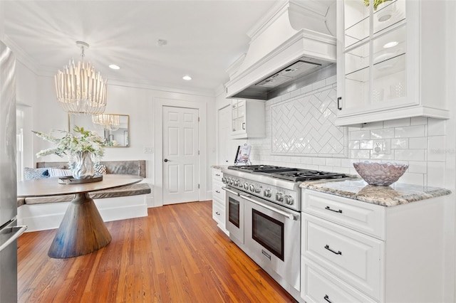 kitchen with premium range hood, decorative light fixtures, white cabinetry, double oven range, and breakfast area