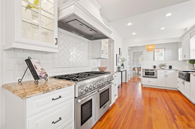 kitchen featuring appliances with stainless steel finishes, white cabinets, custom exhaust hood, ornamental molding, and light stone counters