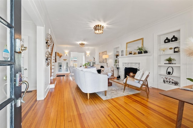 living room featuring ornamental molding, built in features, and light wood-type flooring