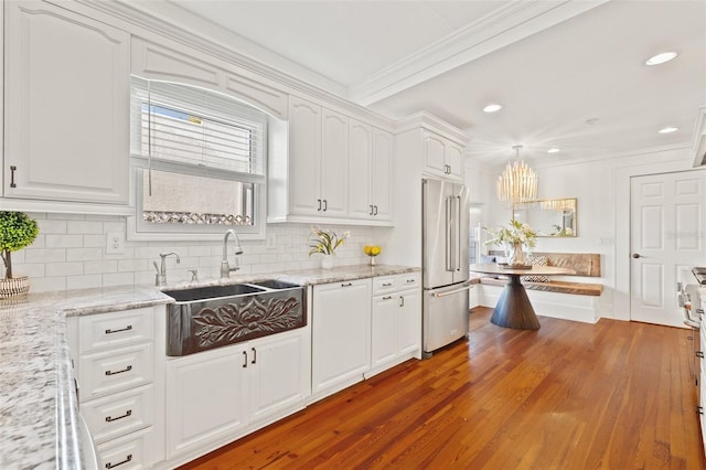 kitchen featuring white cabinetry, high quality fridge, sink, and light stone counters