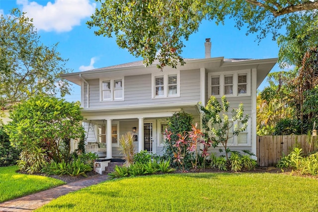 view of front of home with a porch, a chimney, a front lawn, and fence