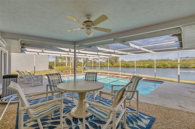 view of swimming pool featuring ceiling fan, a water view, glass enclosure, and a patio area