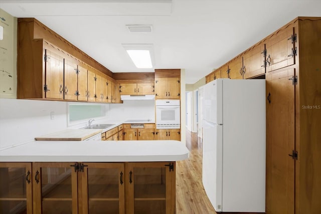 kitchen with white appliances, kitchen peninsula, sink, and light hardwood / wood-style flooring