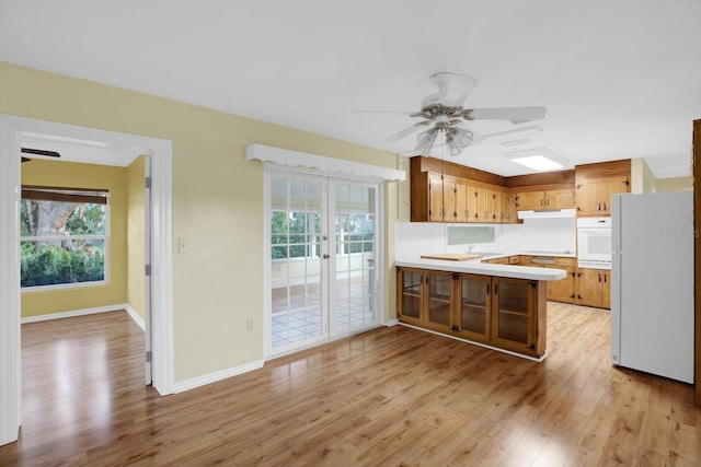 kitchen with white appliances, plenty of natural light, kitchen peninsula, and light wood-type flooring