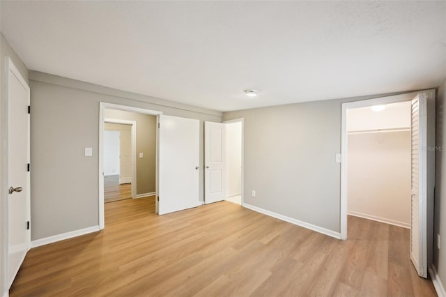 unfurnished bedroom featuring a spacious closet, a closet, and light wood-type flooring