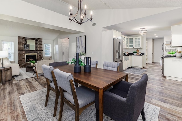 dining space featuring lofted ceiling, an inviting chandelier, a wealth of natural light, light hardwood / wood-style floors, and a brick fireplace