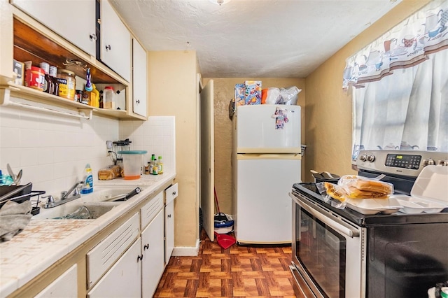 kitchen featuring dark parquet flooring, sink, white cabinetry, stainless steel range with electric stovetop, and white fridge