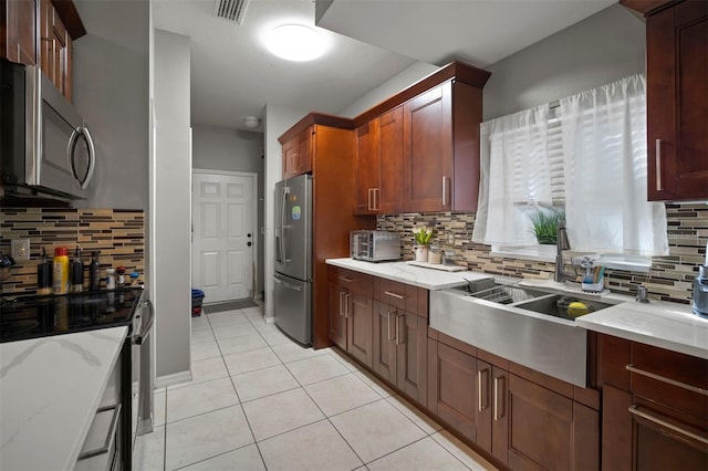 kitchen with sink, light tile patterned floors, stainless steel appliances, light stone countertops, and decorative backsplash