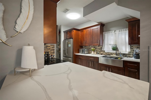 kitchen featuring stainless steel refrigerator with ice dispenser, light stone countertops, sink, and tasteful backsplash