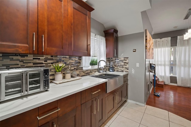 kitchen with sink, light tile patterned floors, backsplash, light stone countertops, and decorative light fixtures