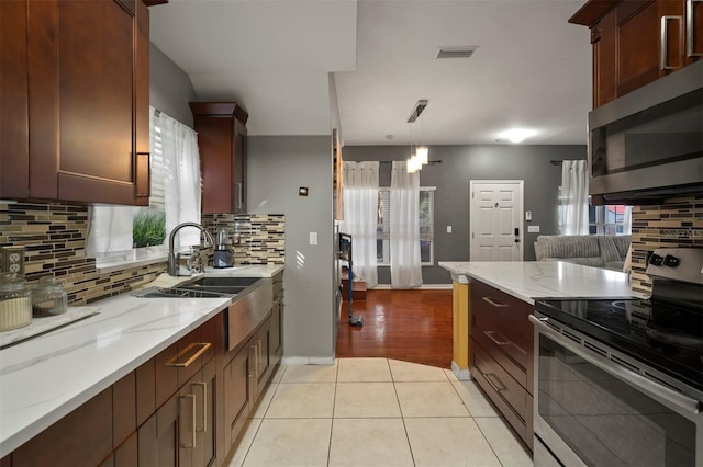 kitchen featuring light stone counters, light tile patterned floors, appliances with stainless steel finishes, pendant lighting, and decorative backsplash