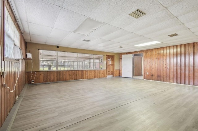 empty room featuring a paneled ceiling, wooden walls, and light wood-type flooring