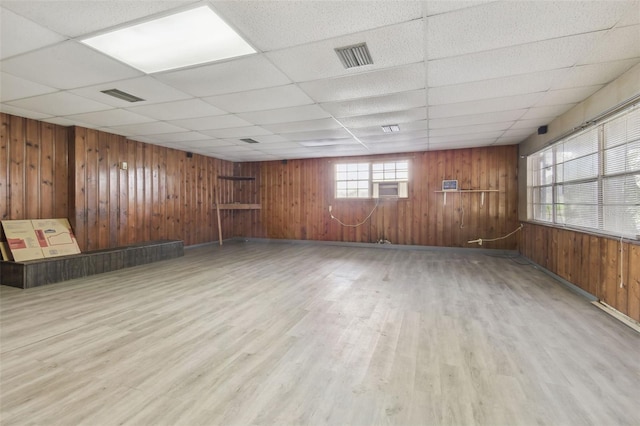 empty room with wood walls, a paneled ceiling, and light wood-type flooring