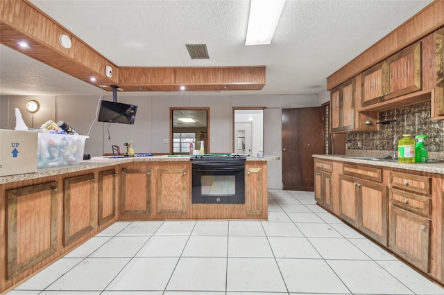 kitchen featuring light tile patterned flooring, black range oven, sink, backsplash, and a textured ceiling