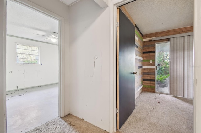 corridor with light colored carpet, a textured ceiling, and wood walls