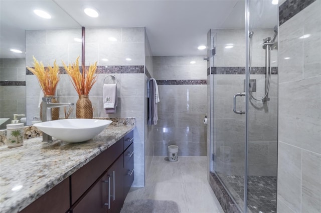 bathroom featuring a shower with door, vanity, and tile walls