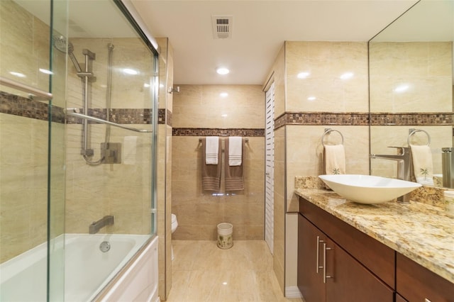 full bathroom featuring toilet, vanity, bath / shower combo with glass door, and tile walls