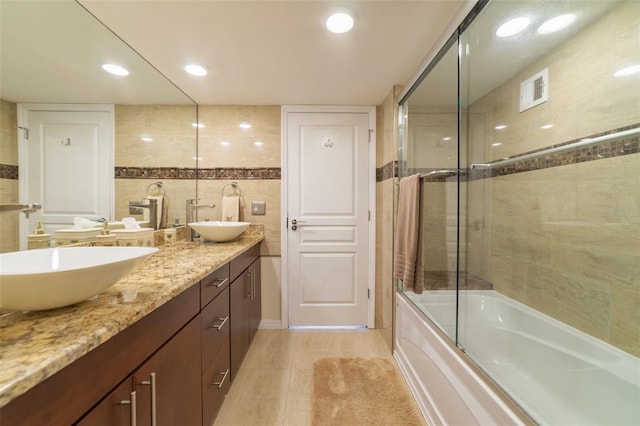 bathroom featuring tile patterned flooring, enclosed tub / shower combo, tile walls, and vanity