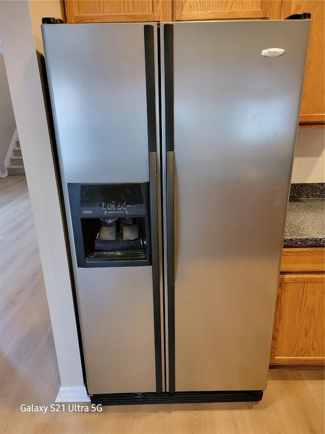 room details with dark stone countertops, light hardwood / wood-style flooring, and stainless steel refrigerator with ice dispenser