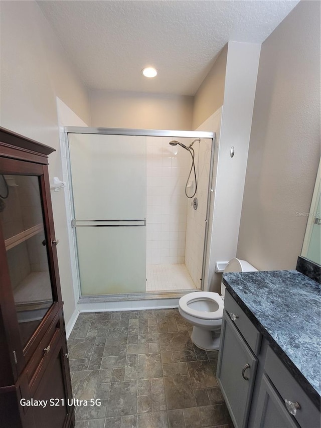 bathroom with an enclosed shower, vanity, toilet, and a textured ceiling