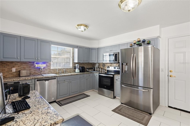 kitchen featuring sink, gray cabinetry, stainless steel appliances, light stone counters, and decorative backsplash