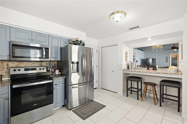 kitchen with gray cabinetry, light stone counters, a breakfast bar area, and appliances with stainless steel finishes