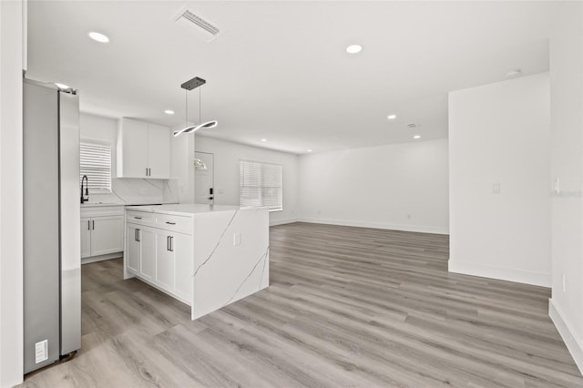 kitchen with stainless steel refrigerator, white cabinetry, decorative backsplash, hanging light fixtures, and light hardwood / wood-style flooring