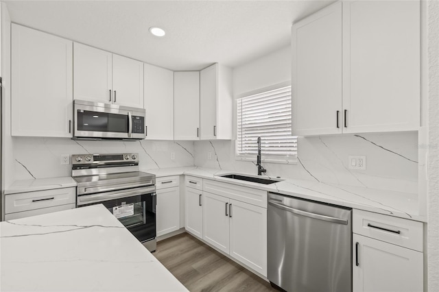 kitchen featuring sink, white cabinetry, light hardwood / wood-style flooring, stainless steel appliances, and light stone countertops