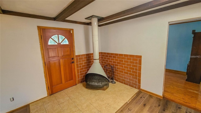 entrance foyer featuring beam ceiling, light wood-type flooring, and a wood stove