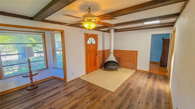 unfurnished living room with beamed ceiling, a wealth of natural light, light wood-type flooring, and a wood stove