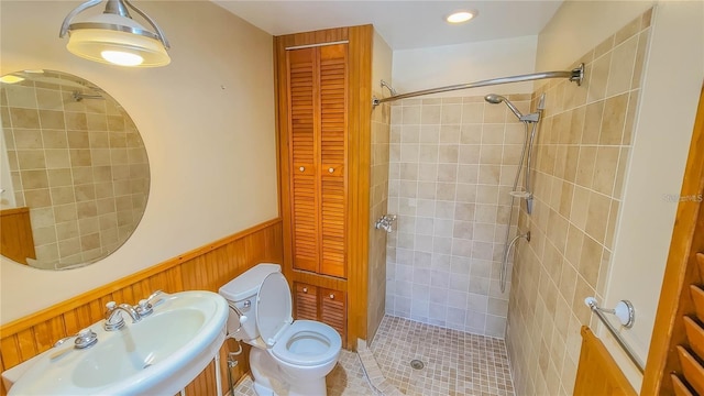 bathroom with wood walls, toilet, sink, and a tile shower