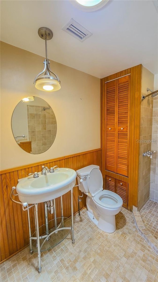 bathroom with tiled shower, wooden walls, and toilet