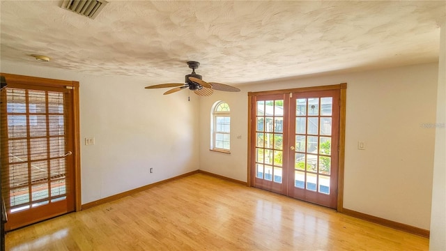 empty room featuring ceiling fan, light hardwood / wood-style flooring, french doors, and a textured ceiling