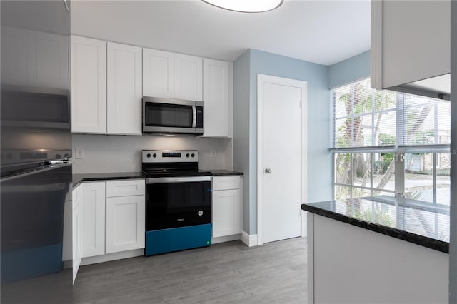 kitchen with appliances with stainless steel finishes, white cabinets, dark stone counters, decorative backsplash, and light hardwood / wood-style floors