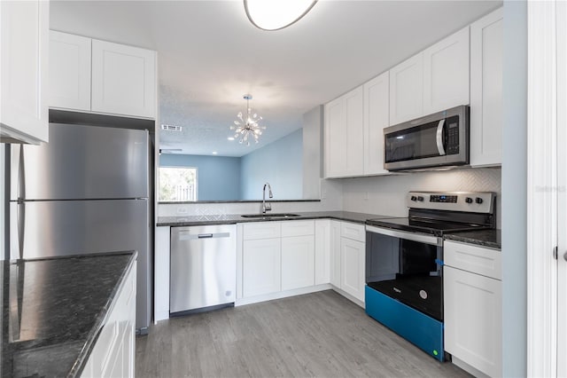 kitchen with appliances with stainless steel finishes, sink, white cabinets, dark stone counters, and light wood-type flooring