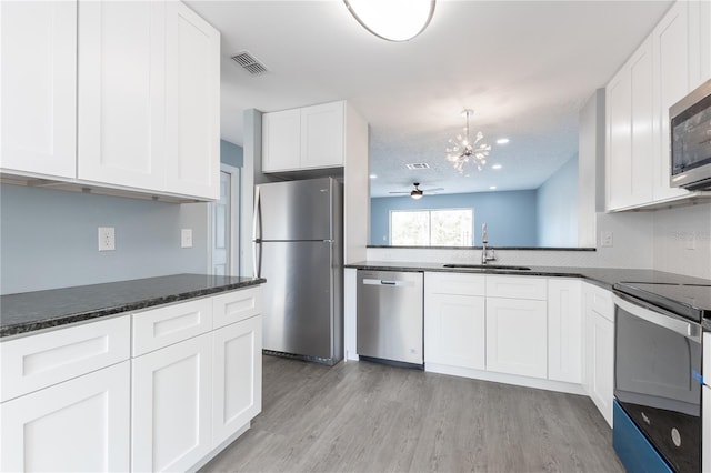 kitchen featuring sink, appliances with stainless steel finishes, white cabinetry, dark stone countertops, and light wood-type flooring