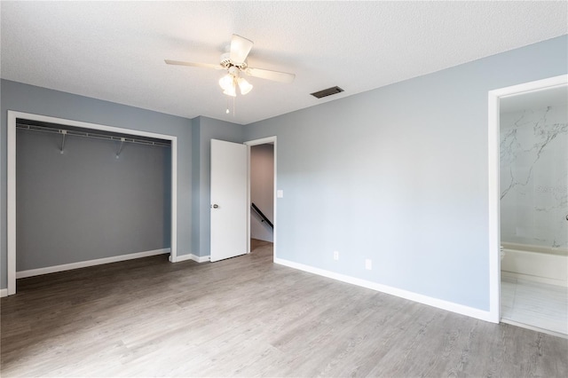 unfurnished bedroom featuring ceiling fan, ensuite bathroom, light hardwood / wood-style floors, a textured ceiling, and a closet