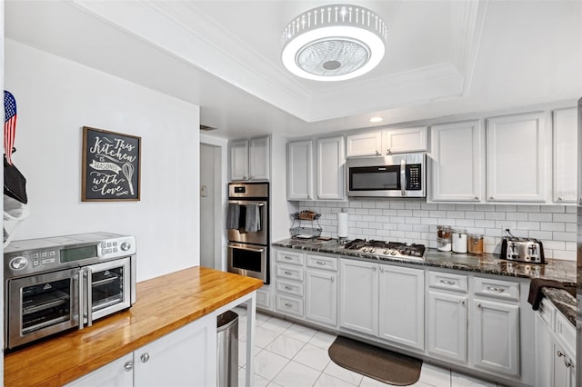 kitchen with tasteful backsplash, appliances with stainless steel finishes, butcher block countertops, and a tray ceiling