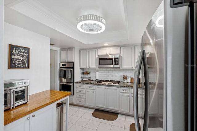 kitchen featuring crown molding, wooden counters, a tray ceiling, stainless steel appliances, and decorative backsplash