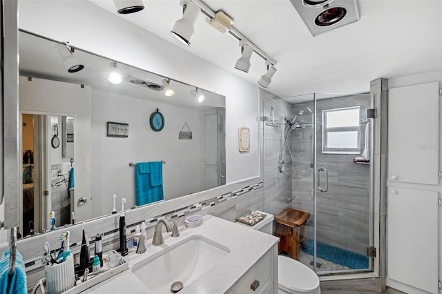 bathroom with tile walls, vanity, track lighting, a shower with shower door, and toilet