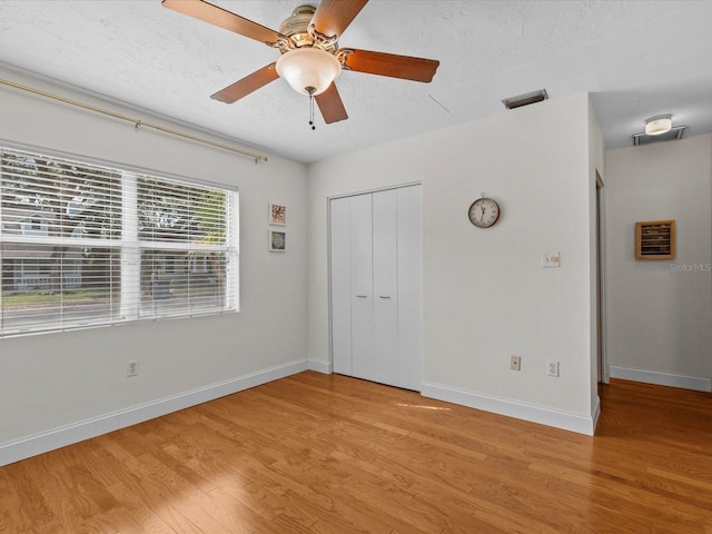 unfurnished bedroom with ceiling fan, a closet, light hardwood / wood-style flooring, and a textured ceiling