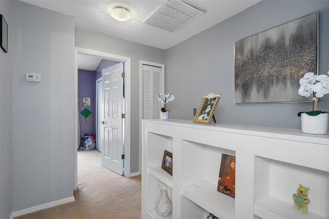 hall featuring light carpet and a textured ceiling