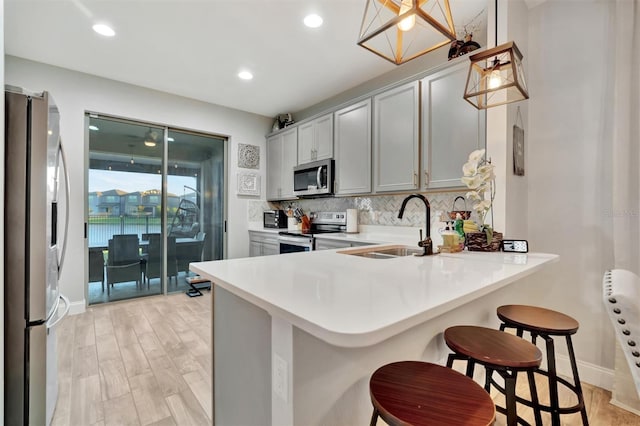 kitchen with decorative light fixtures, a breakfast bar area, gray cabinetry, kitchen peninsula, and stainless steel appliances