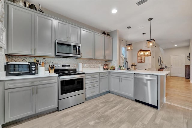 kitchen with appliances with stainless steel finishes, gray cabinets, kitchen peninsula, and decorative light fixtures