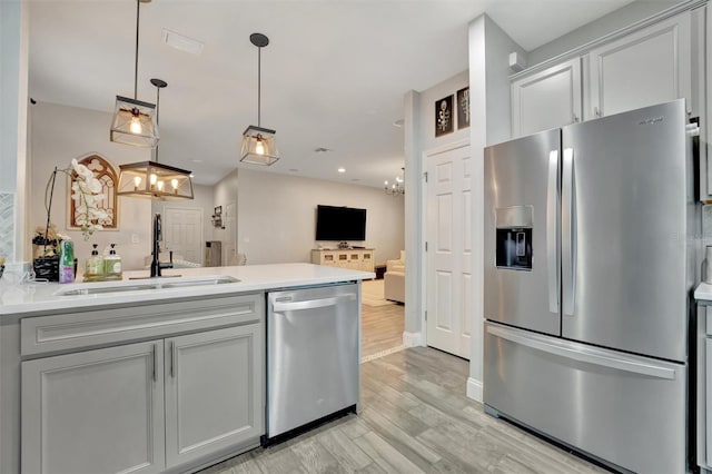 kitchen featuring appliances with stainless steel finishes, sink, hanging light fixtures, light hardwood / wood-style floors, and kitchen peninsula