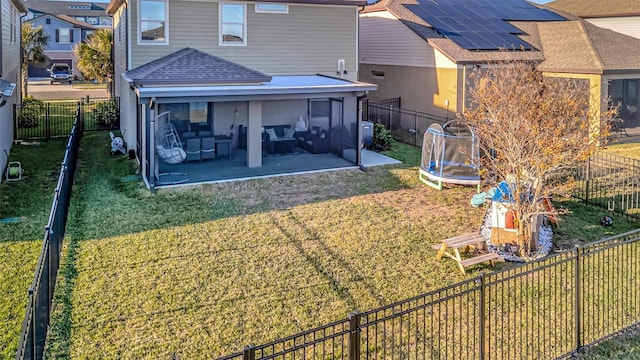 rear view of house with a trampoline, a yard, a patio area, and solar panels